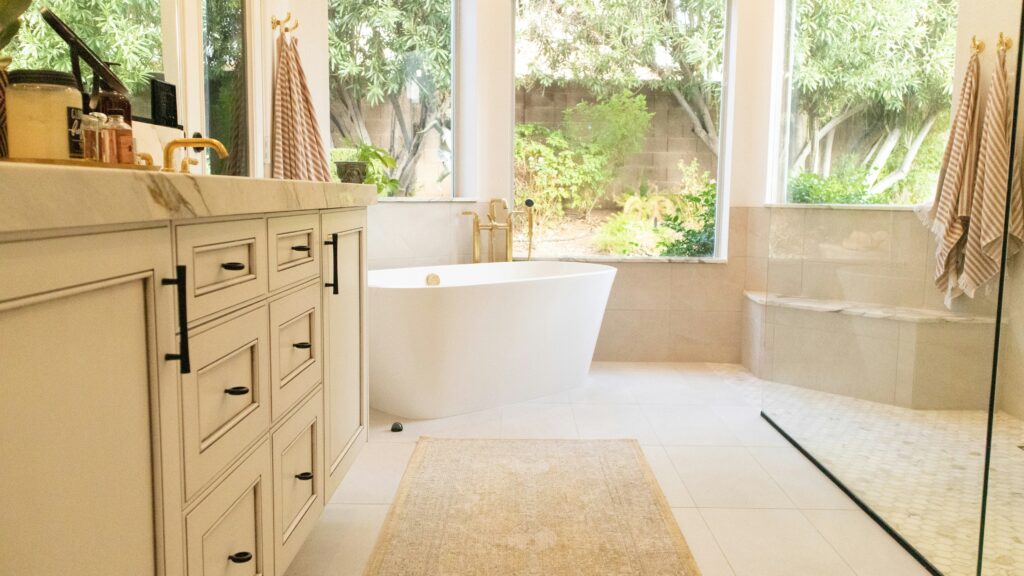 Modern bathroom with large windows, a freestanding bathtub, rainfall showerhead, built-in shelving, and ambient lighting, showcasing bathroom trends for 2024.